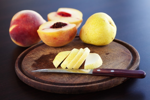 Photo peach, pear and a knife on a cutting board