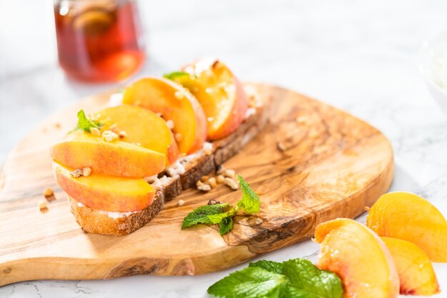 Peach ricotta toast garnished with walnuts and fresh mint on a wooden cutting board.