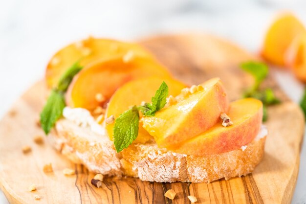 Peach ricotta toast garnished with walnuts and fresh mint on a wooden cutting board.