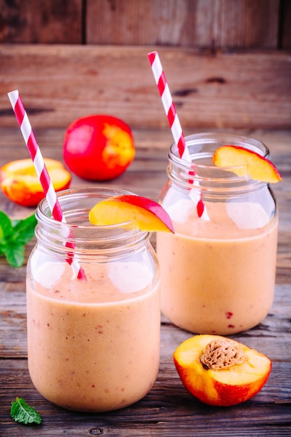 Peach smoothies in a mason jar with mint on wooden rustic background