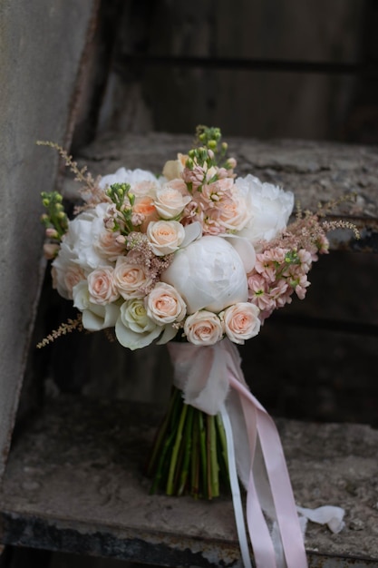 牡丹のバラとアスティルベの結婚式の日で構成される暗い石の背景に桃と白のウェディングブーケ