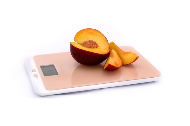 A peach with a cut-out slice on a kitchen scale on a white background.