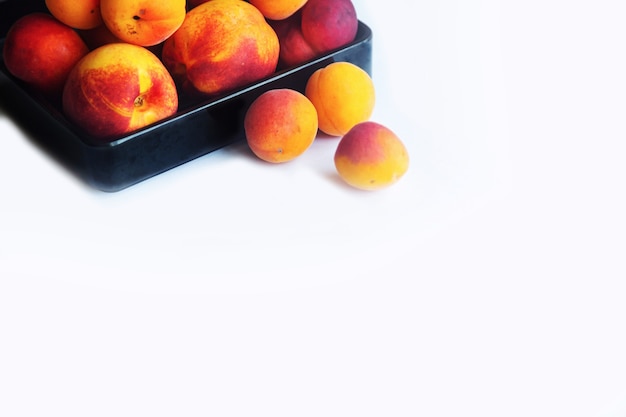 Peaches apricots and nectarines in a black plate on a white background