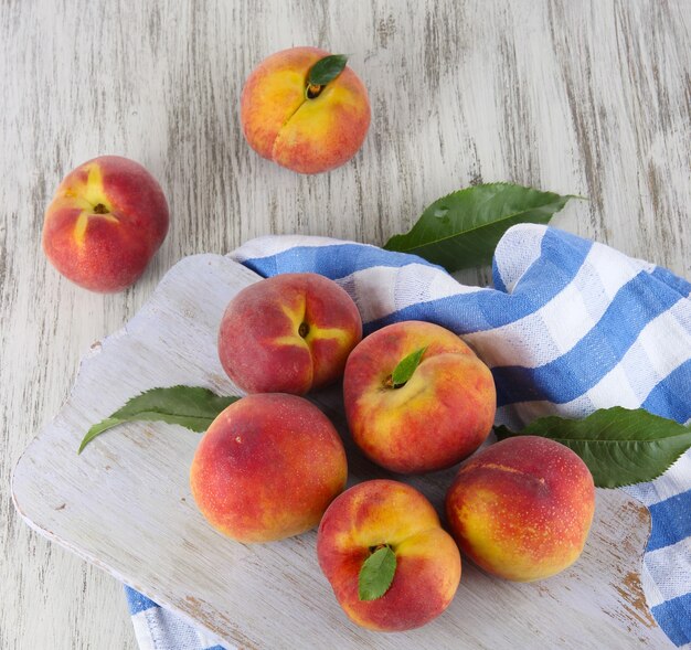 Peaches on board on napkin on table on wooden table, top view