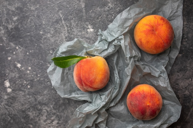 Peaches or nectarines in a gray dark stone plate with leaves, top view