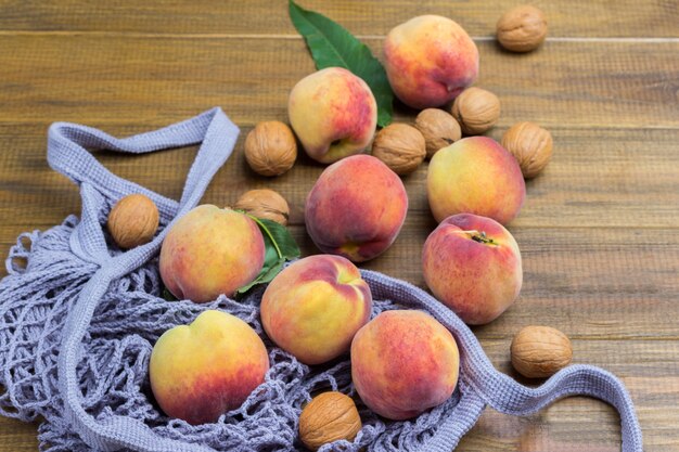 Peaches with green leaves in fabric mesh bag. Wooden background. Top view