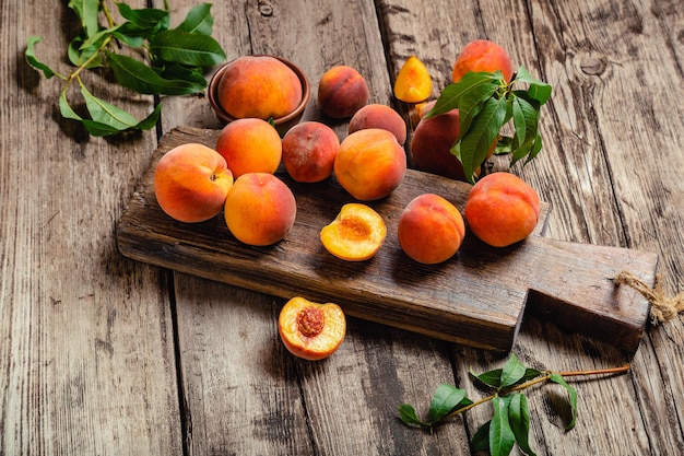 Peaches with leaves on wooden table with peach in halves. Ripe juicy peaches. Harvest of peaches for food or juice. Fresh organic fruit on cutting board.