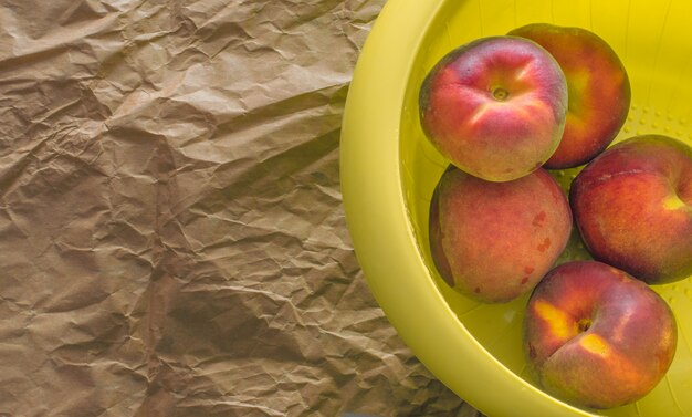 Peaches in a yellow plastic cup on a brown paper