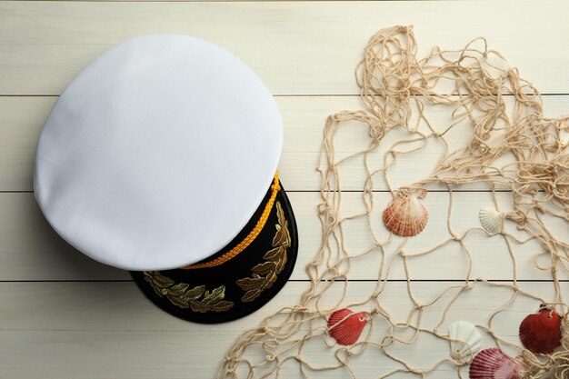 Peaked cap net and shells on white wooden background flat lay