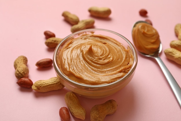 Peanut bowl and spoon with peanut butter on pink background