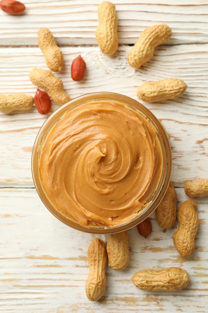 Peanut and bowl with peanut butter on wooden background