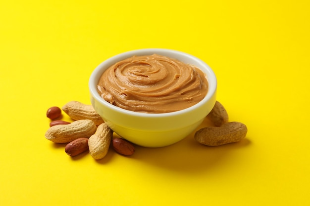 Peanut and bowl with peanut butter on yellow background