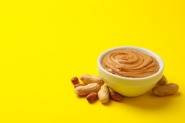 Peanut and bowl with peanut butter on yellow background