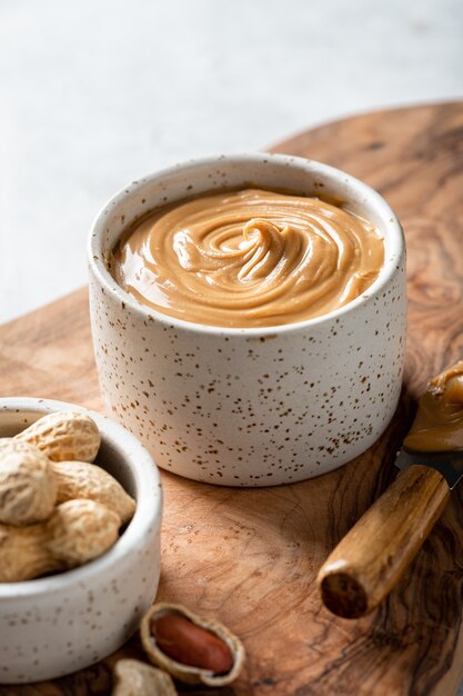 Peanut butter in a ceramic bowl on a wooden cutting board on a light background