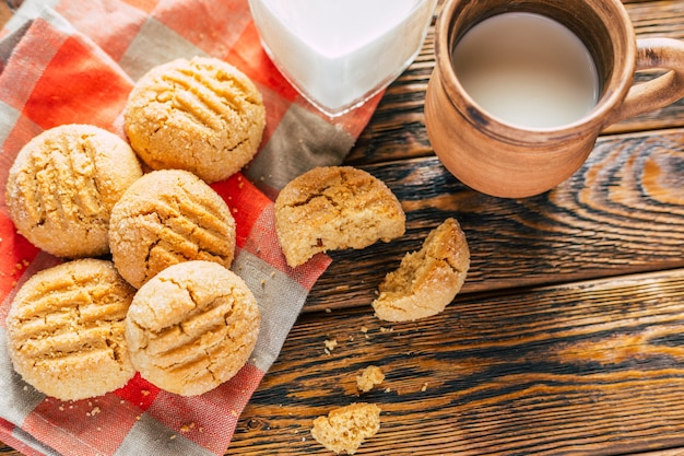 Peanut butter cookies and clay mug with milk on wooden background