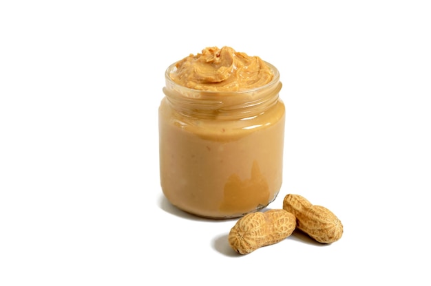 Photo peanut butter in a glass jar with peanuts isolated on white background.  a traditional product of american cuisine.