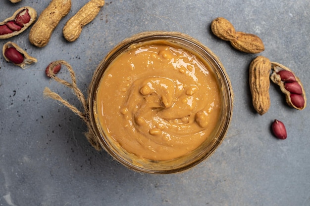 Peanut butter in an open jar creamy peanut butter peanuts scattered top view