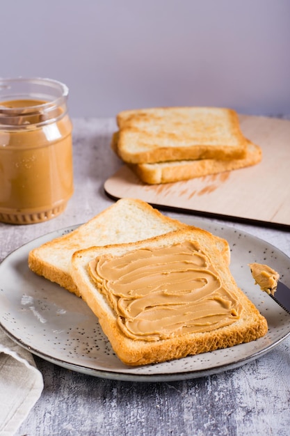 Peanut butter sandwich on toasted bread on a plate and jar of butter on the table Verical view