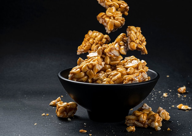 Peanut kozinaki falling in bowl on black background with copy space