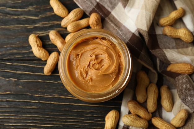 Peanut, napkin and jar with peanut butter on wooden background