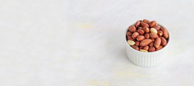 Peanuts in bowl on white wooden background