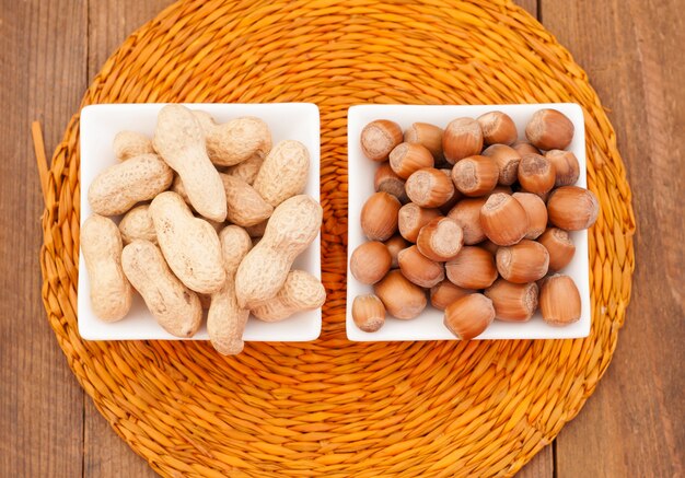 Peanuts and hazelnuts in a white bowl on a wicker napkin