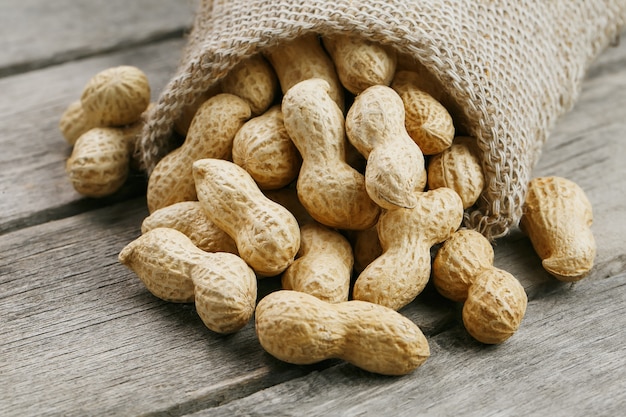 Peanuts in a miniature burlap bag on old, gray wooden surface