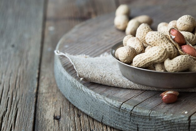 Peanuts in nutshell on wooden bowl