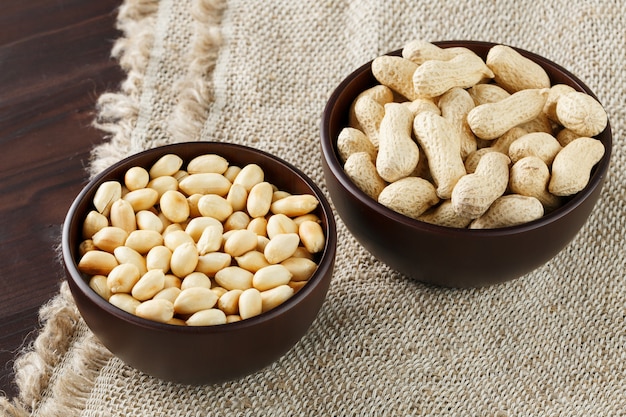 Peanuts in the shell and peeled close-up in cups, Roasted peanuts in their shells and peeled against a brown cloth