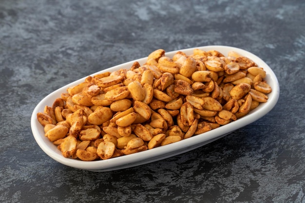 Peanuts with hot sauce on plate on dark background