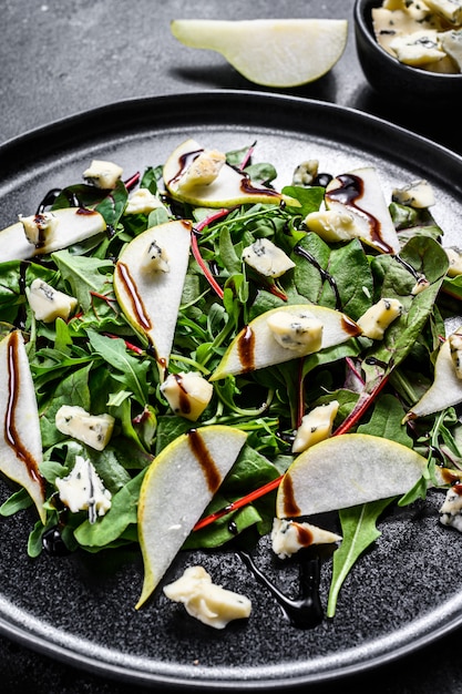 Pear, blue cheese, arugula and nut salad on plate. Black background. Top view