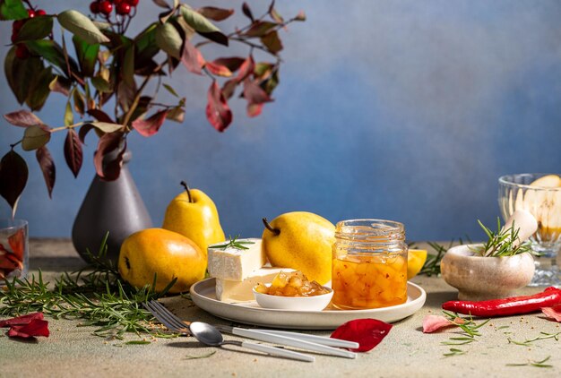 Photo pear jam in jar surrounded by ingredients cheese and herbs