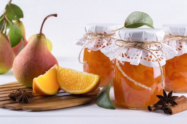 Pear and orange jam in  glass jars with ripe pears, cinnamon sticks, anise stars and green  leaves on the table.