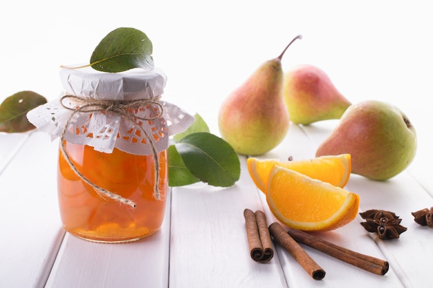 Pear and orange jam in  glass jars with ripe pears, cinnamon sticks, anise stars and green  leaves on the table.
