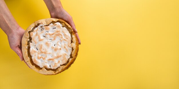 Pear pie on blue napkin in female hands, on yellow. Copy space.