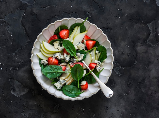 Pear spinach blue cheese strawberry salad on a dark background top view