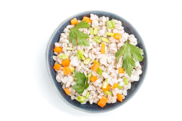Pearl barley porridge with vegetables in blue ceramic bowl isolated on white surface. Top view, close up.