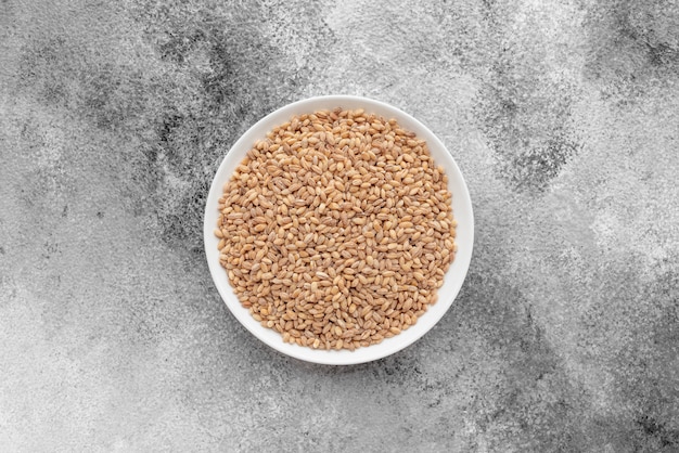 Pearl barley in a white saucer on a gray concrete background