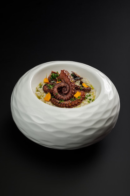 Pearl barley with octopus tentacles in big white plate isolated over black background