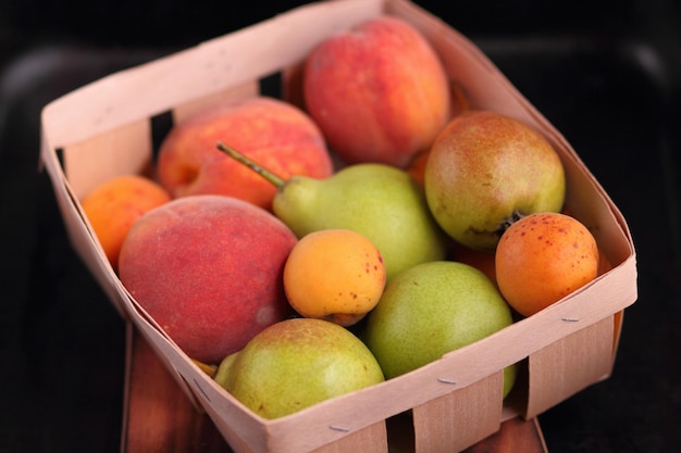 Pears apricots and peaches in a wooden basket on a wooden board on a dark background Beautiful composition of juicy fruits Closeup