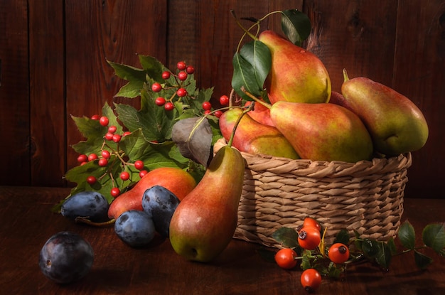 Photo pears in a basket and branches of wild rose and viburnum on a dark wooden background in a rustic style