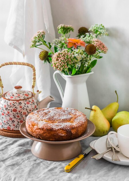 Грушевый пирог и сахарная пудра, букет цветов, чайник, сервированный стол для чая
