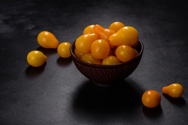 Pearshaped small yellow tomatoes in a ceramic plate on a dark concrete table