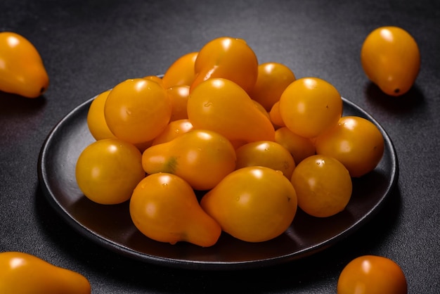 Pearshaped small yellow tomatoes in a ceramic plate on a dark concrete table