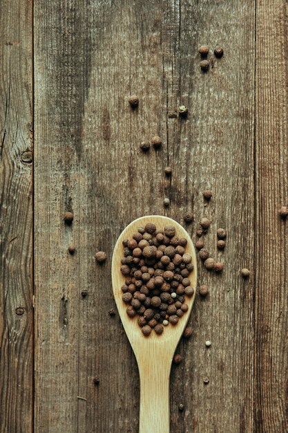熟した木製テーブルの上の木のスプーンで香りの良いコショウのエンドウ豆