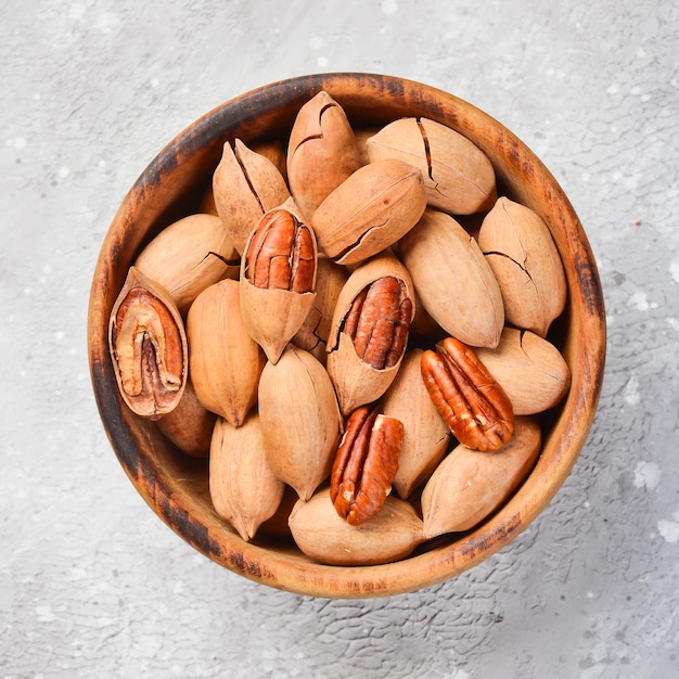 Pecannoten Pecannoten in de schaal in een kom Op een stenen ondergrond Pecannoten zijn rijk aan verschillende sporenelementen en vitamines