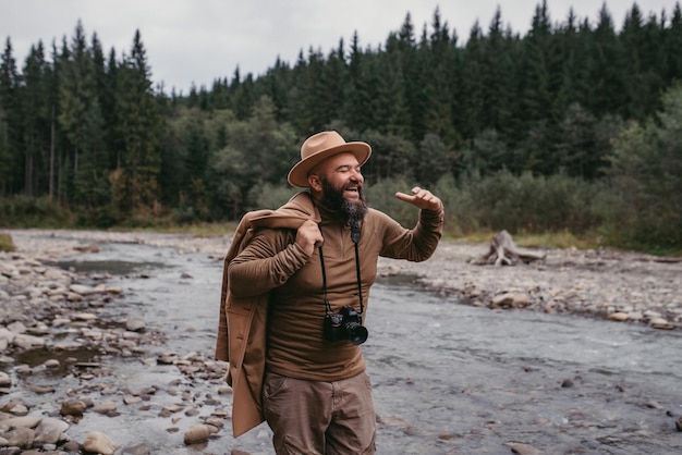 Pedestrian guy standing on the rocks of the river with a professional camera in his hands