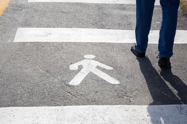 Pedestrian sign on the asphalt and human legs walking on sunny day