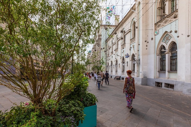 Pedestrian street decorated with blooming flowers bushes trees with people walking Moscow Russia