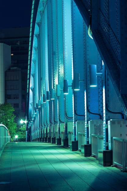 Pedestrian way along the metallic arc structure of city bridge illuminated by night